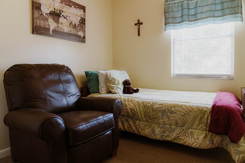 A cozy bedroom with a leather chair, a bed, and wall decorations including a map and a cross.