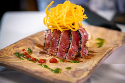 A beautifully plated dish featuring seared tuna topped with crispy noodles and drizzled with vibrant sauces.