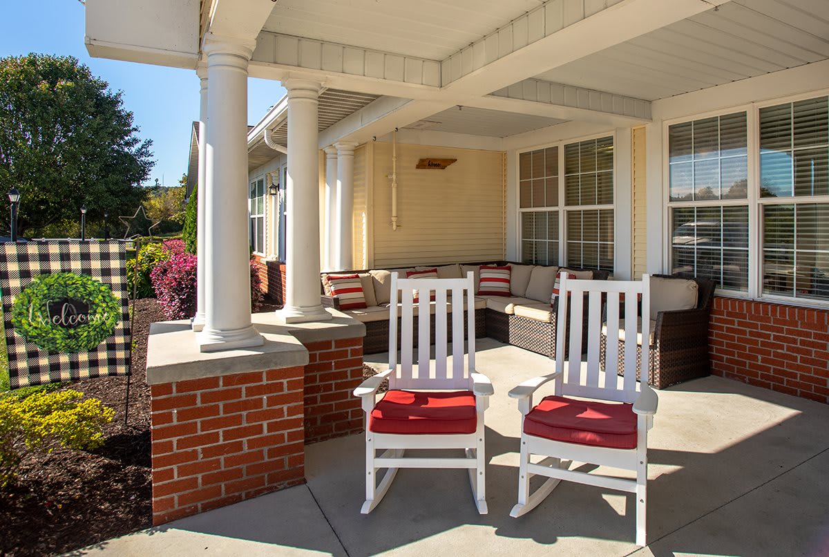 A cozy porch with two white rocking chairs featuring red cushions, surrounded by columns and a brick wall.