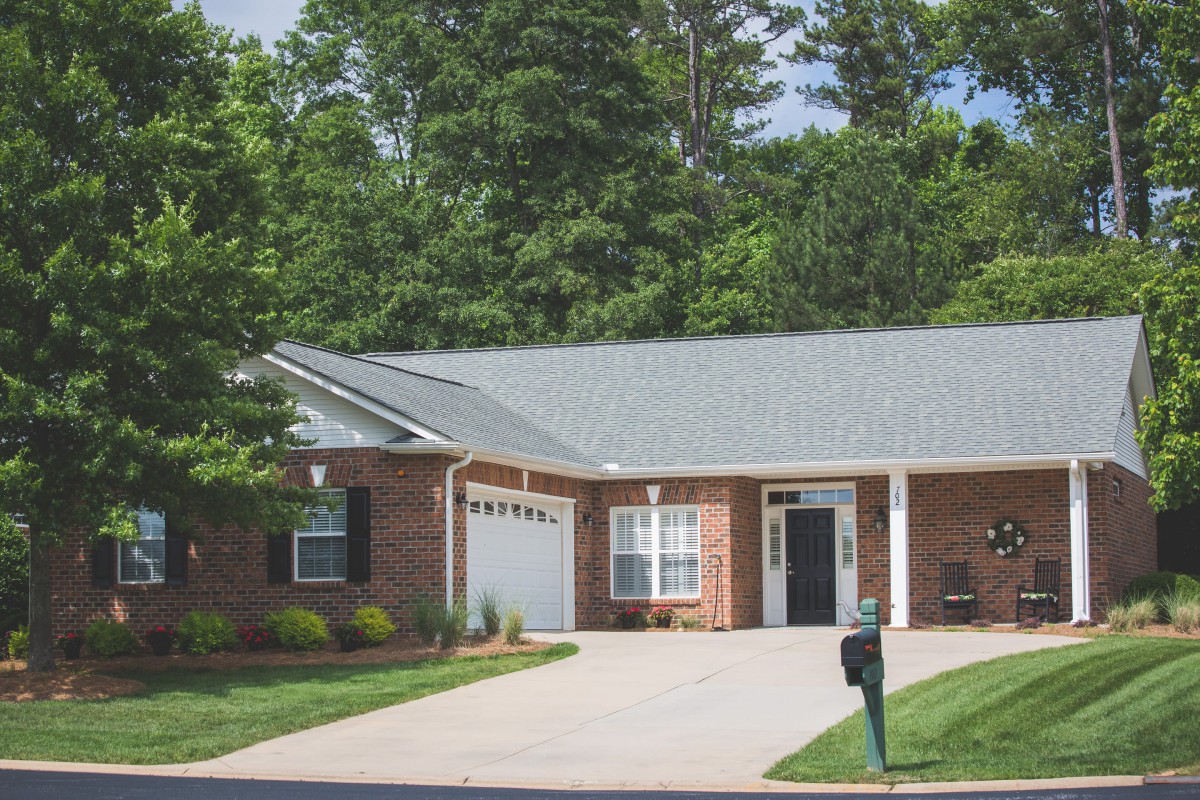 A suburban brick house with a driveway and garage, surrounded by trees.