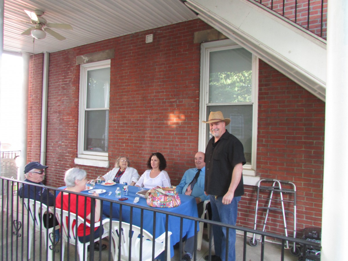 A group of people enjoying a meal together on a patio next to a brick house.