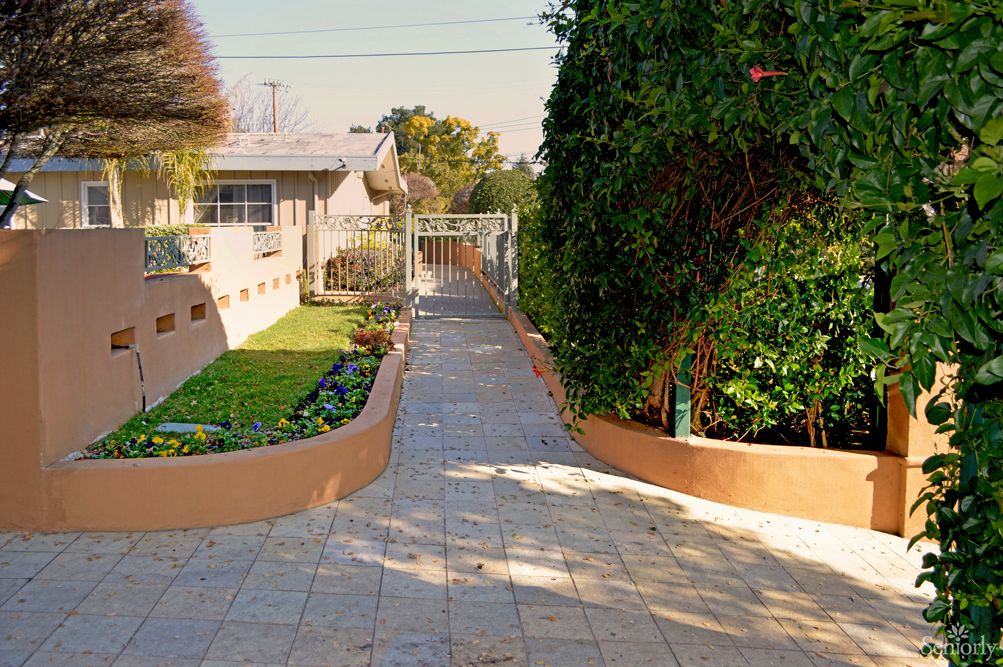 A landscaped pathway bordered by garden areas and trees, leading to a house.