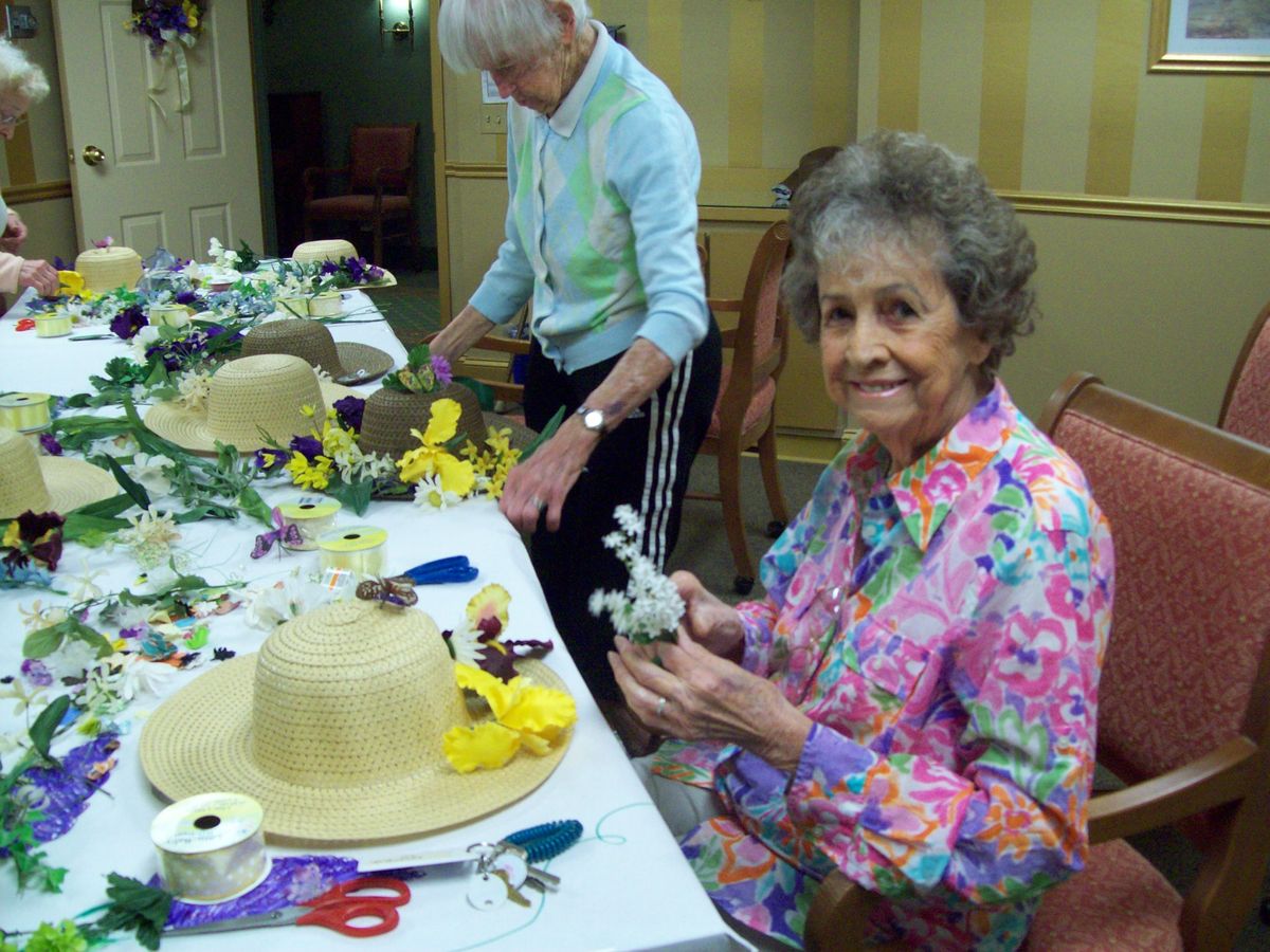 Elderly women engaged in a hat decorating craft session with flowers and other materials.
