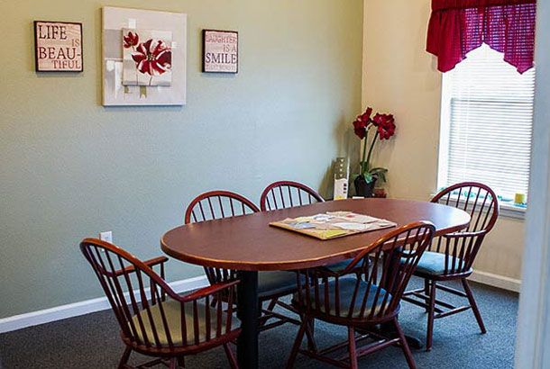 A cozy dining area with a wooden table surrounded by chairs, adorned with wall art and a window with red curtains.