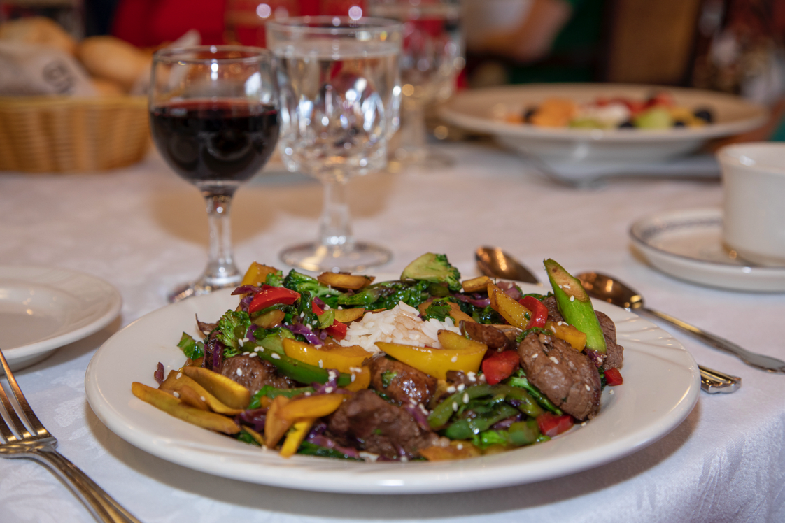A gourmet dinner featuring a colorful vegetable and steak dish paired with a glass of red wine.