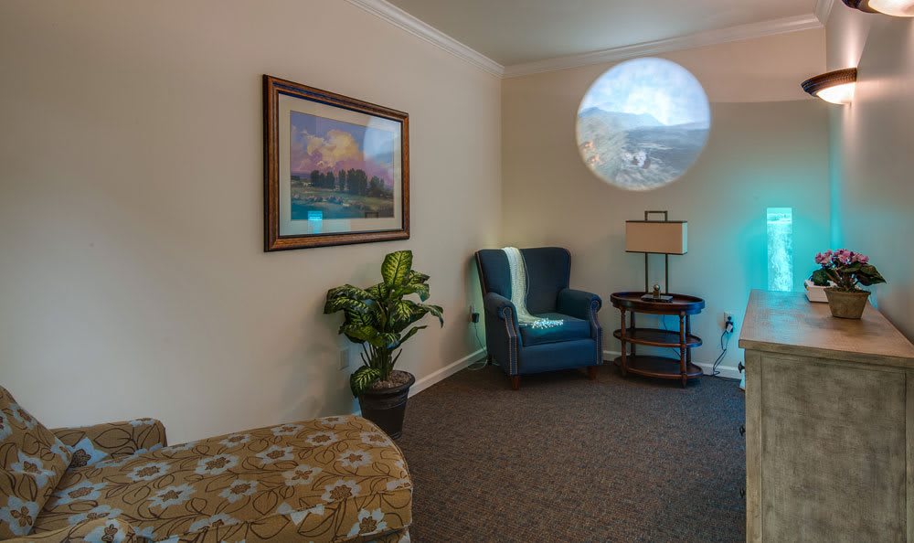 A cozy living room with an armchair, lamp, plant, and artwork on the wall.