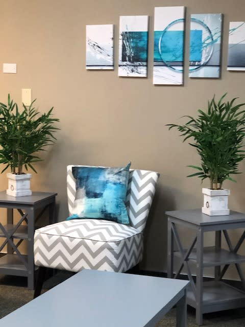A cozy living room corner featuring a patterned chair, side tables with potted plants, and artwork on the wall.