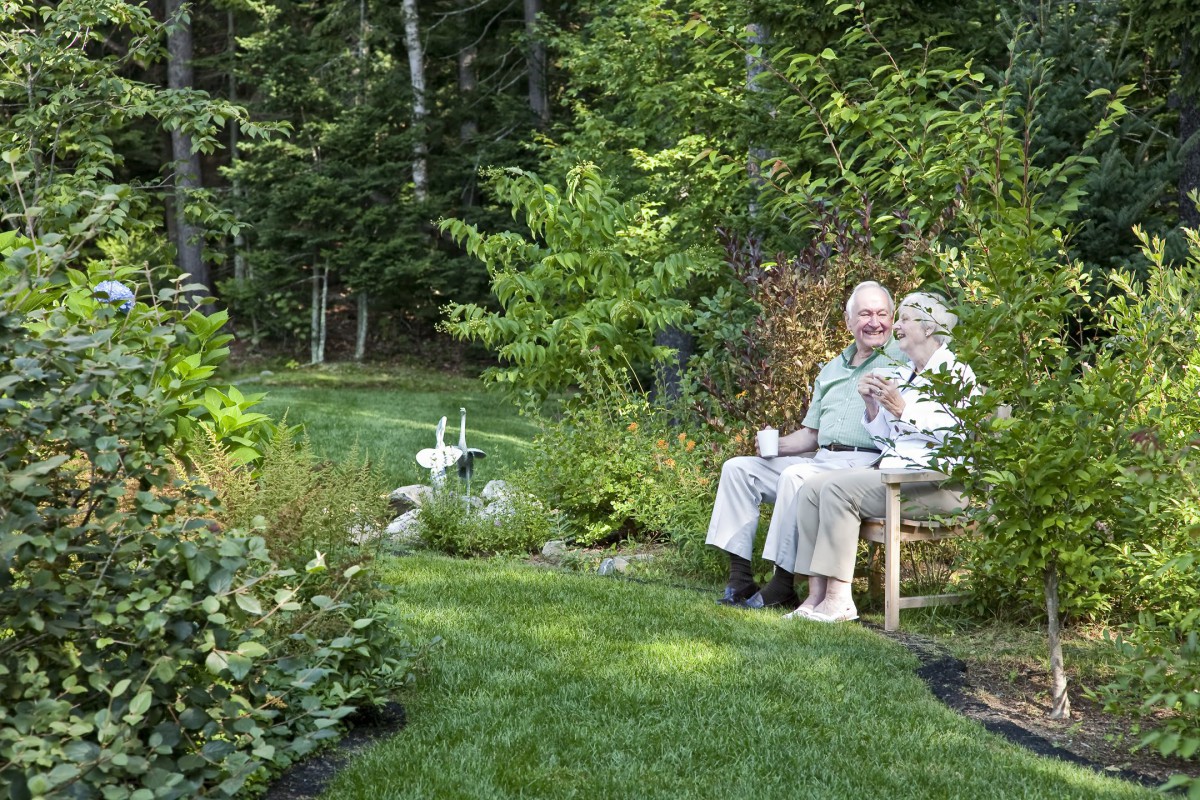 An elderly couple sitting on a bench in a lush garden.