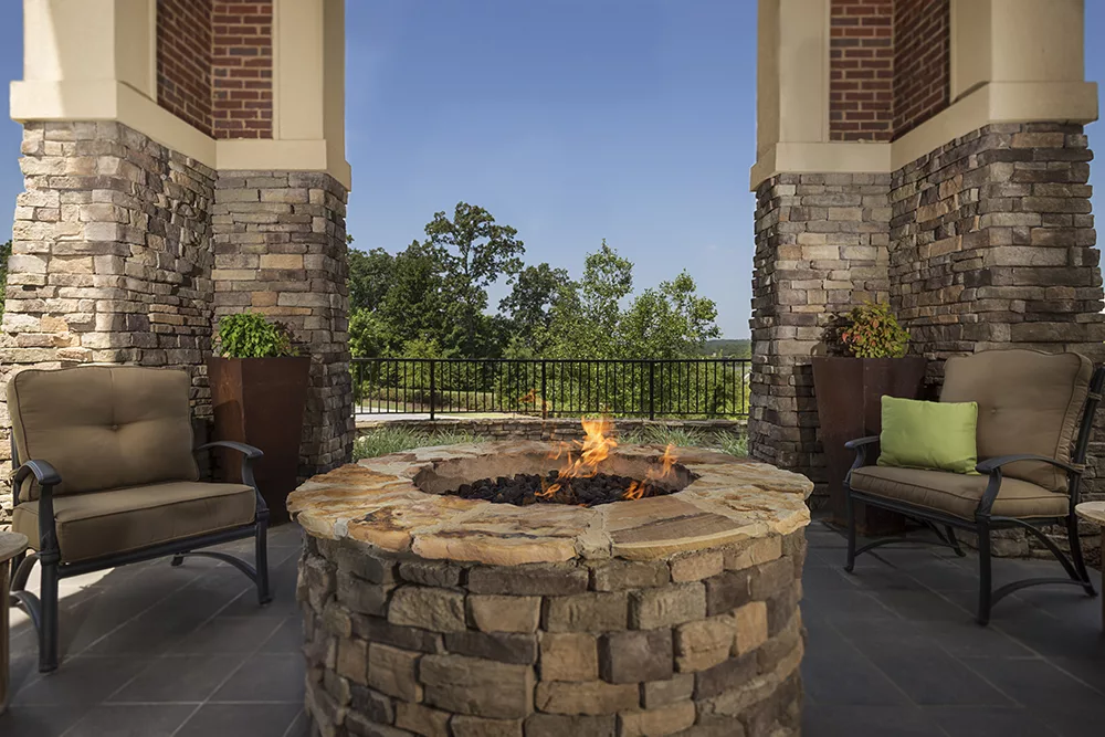 An outdoor patio with a stone fire pit and a scenic view of trees.