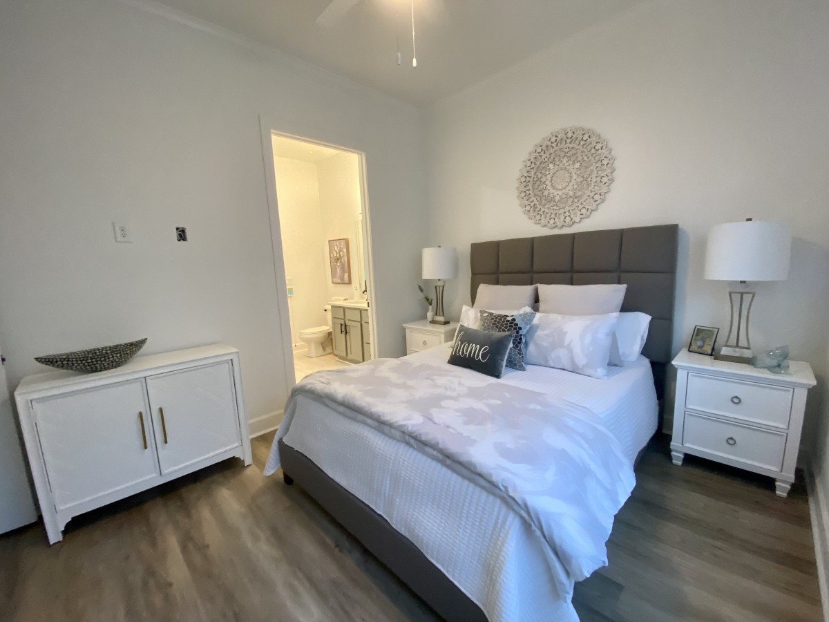 A modern bedroom with a neatly made bed, white walls, and wooden flooring, featuring stylish nightstands and decorative art.
