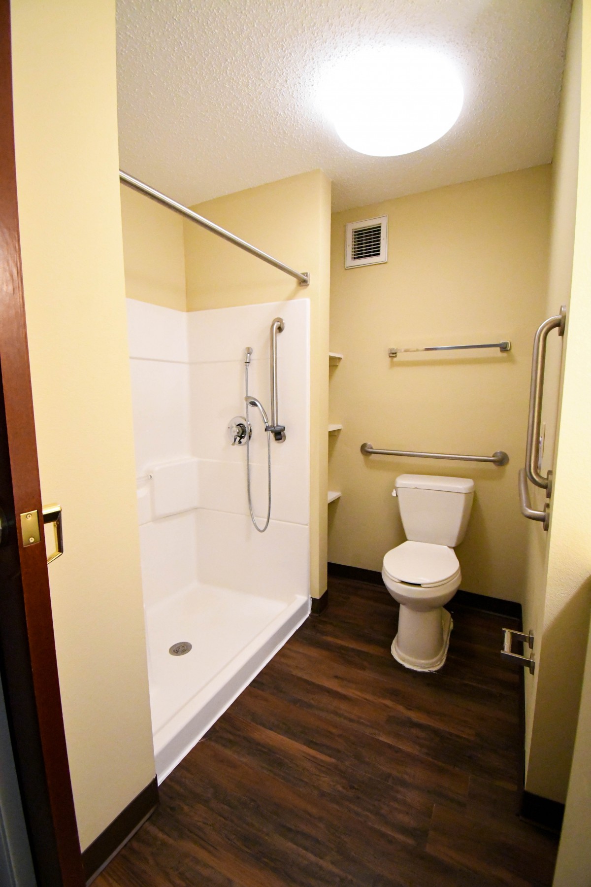 An accessible bathroom featuring a shower with handrails and a toilet.