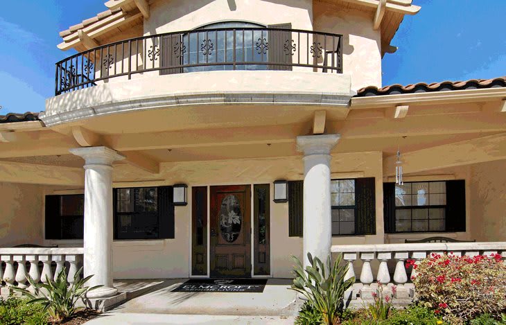 A two-story house with a front porch and balcony featuring columns and decorative railings.