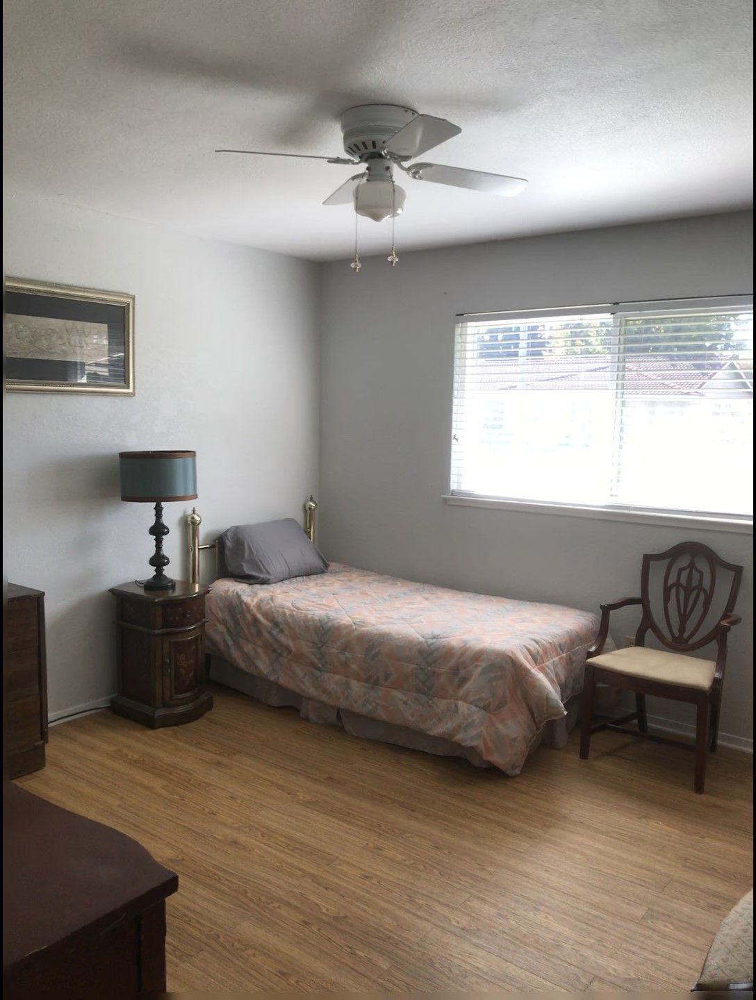 A simple bedroom with a single bed, chair, and lamp near a window.