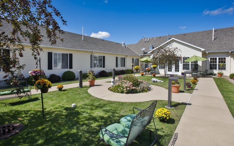 A beautiful garden with a well-maintained lawn and outdoor seating on a sunny day, surrounded by residential buildings.