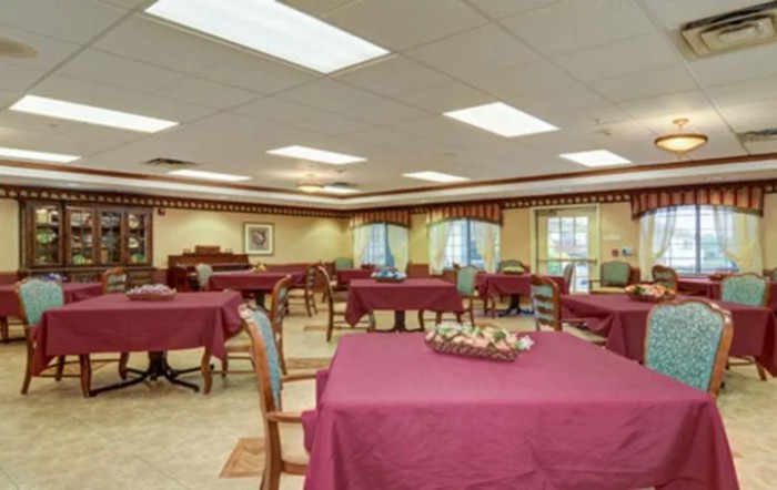 An indoor dining area with tables covered in burgundy tablecloths and wooden chairs.