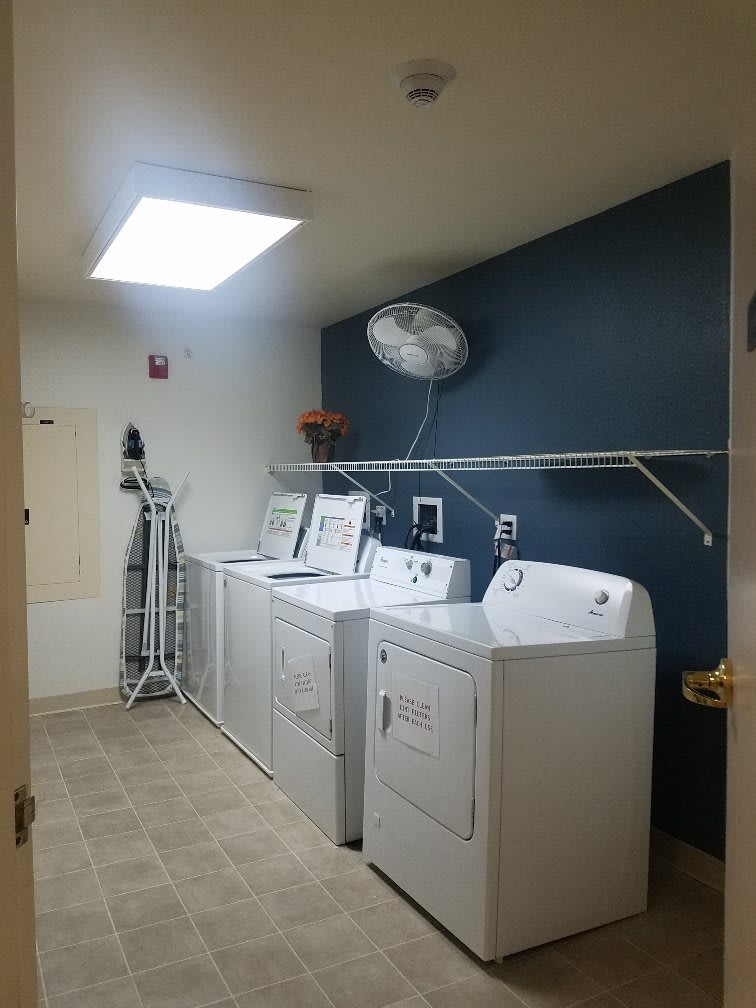 A laundry room with washing machines, dryers, and an ironing board.