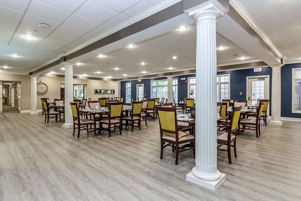 A spacious dining area with elegant columns and neatly arranged tables and chairs under bright lighting.