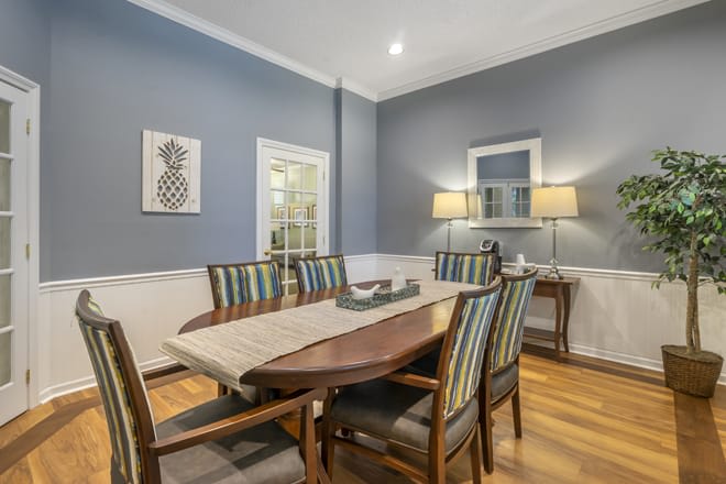 Elegant dining room with a large table and striped chairs, complemented by wall art and a warm lamp.