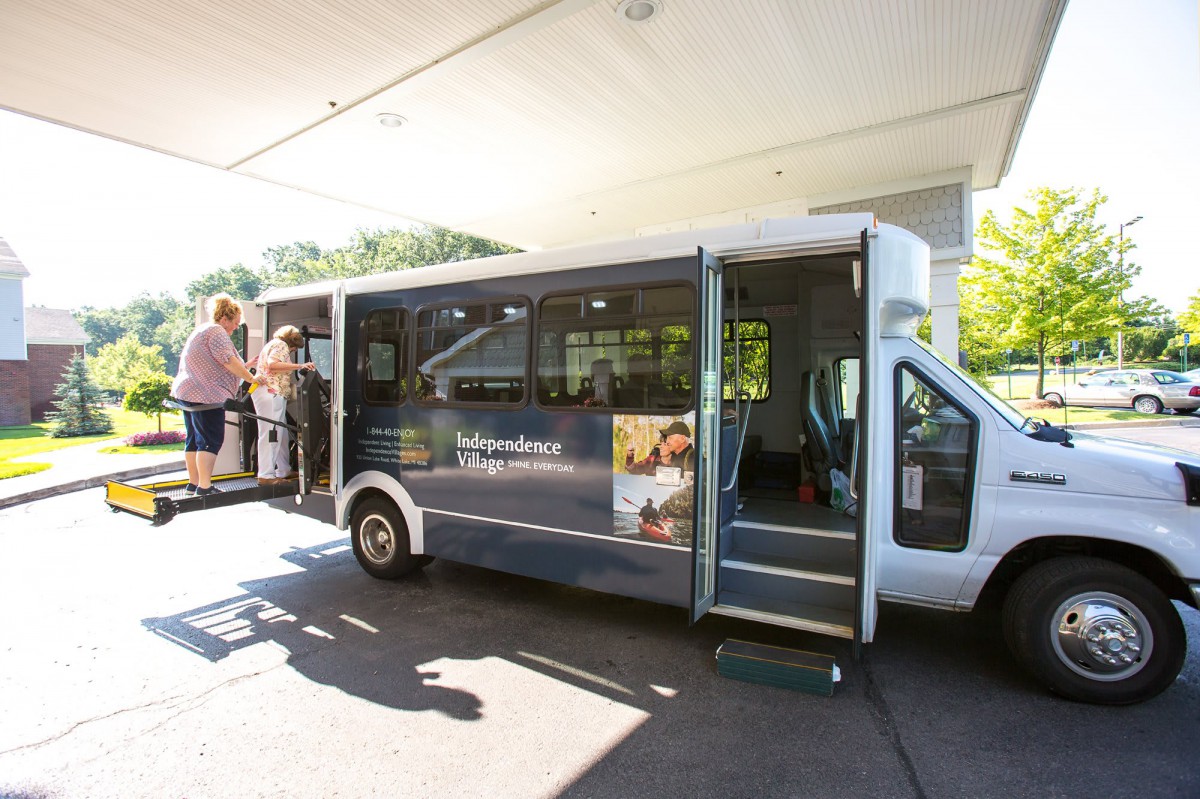 A small shuttle bus picking up passengers at a station during the day.