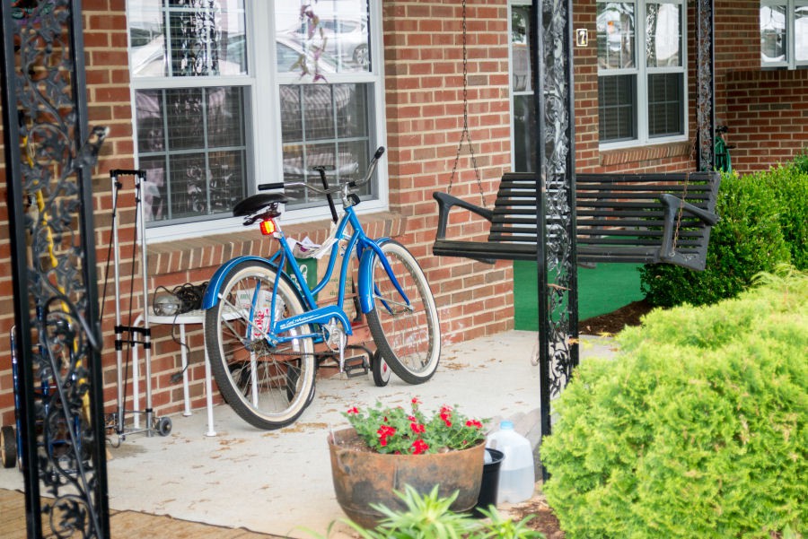 A cozy porch with a blue bicycle, a swing, and a blooming planter.