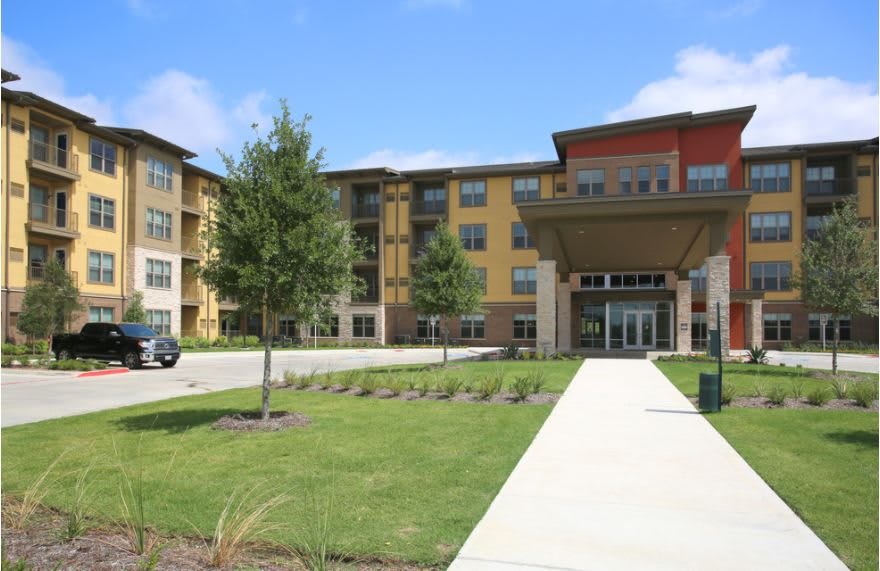 A modern residential building with a landscaped entrance and well-maintained lawn.