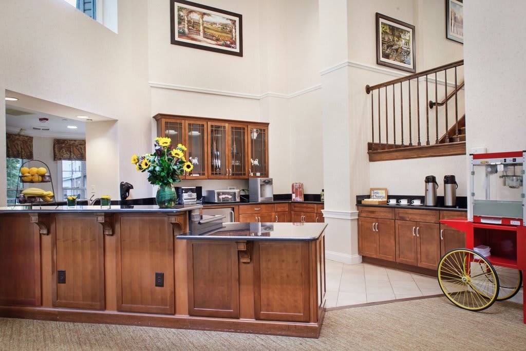 A modern kitchen interior featuring wooden cabinets, a central countertop with a vase of flowers, and an adjacent staircase.