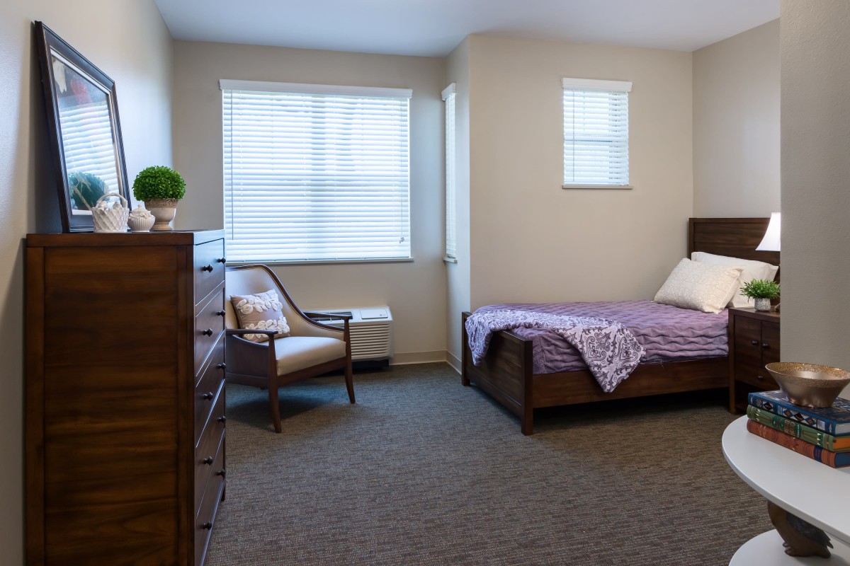A neatly arranged bedroom with a bed, chair, dresser, and windows.