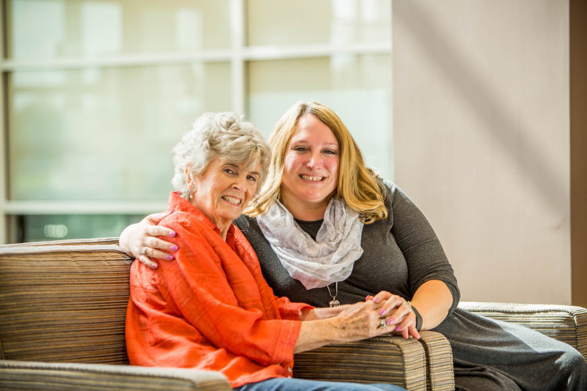 Two women sitting together, smiling and enjoying each other's company indoors.