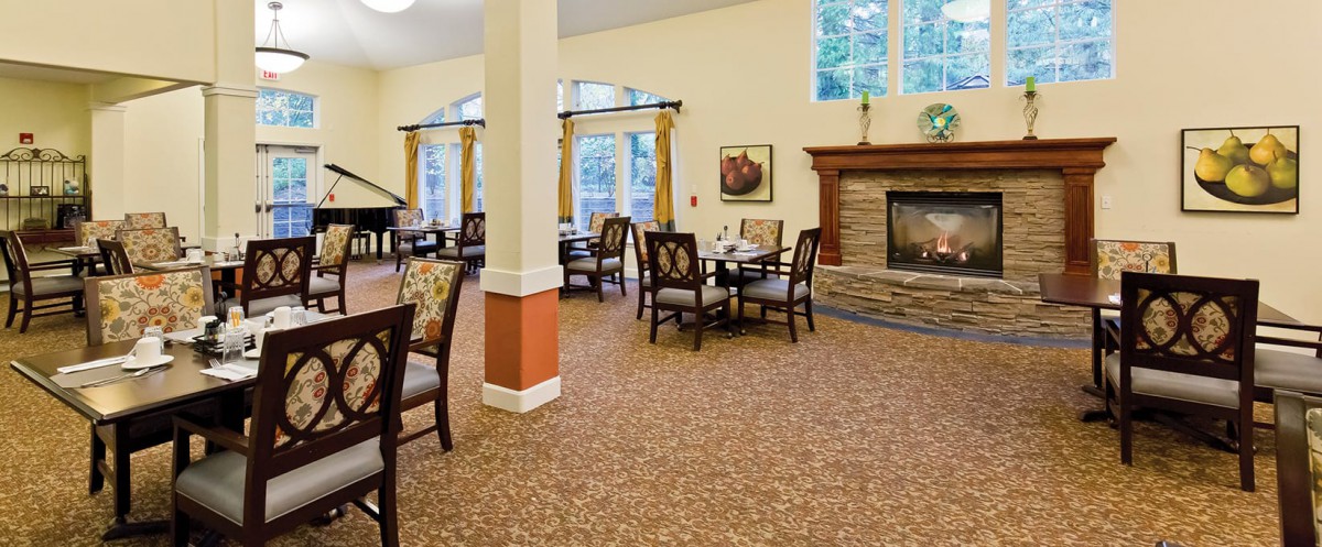 A cozy dining area with a fireplace, featuring tables and chairs, surrounded by large windows.