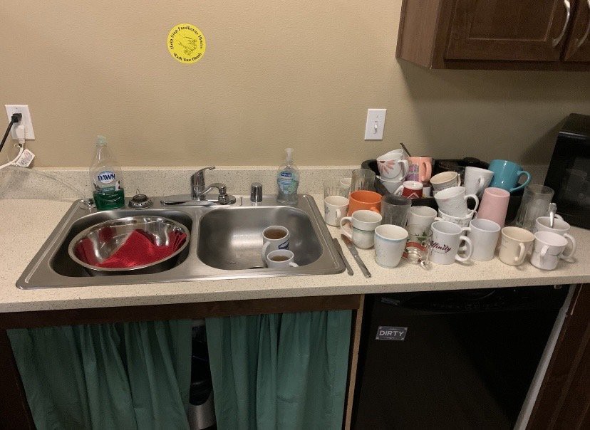 A cluttered kitchen sink with a pile of dirty dishes and mugs on the countertop.