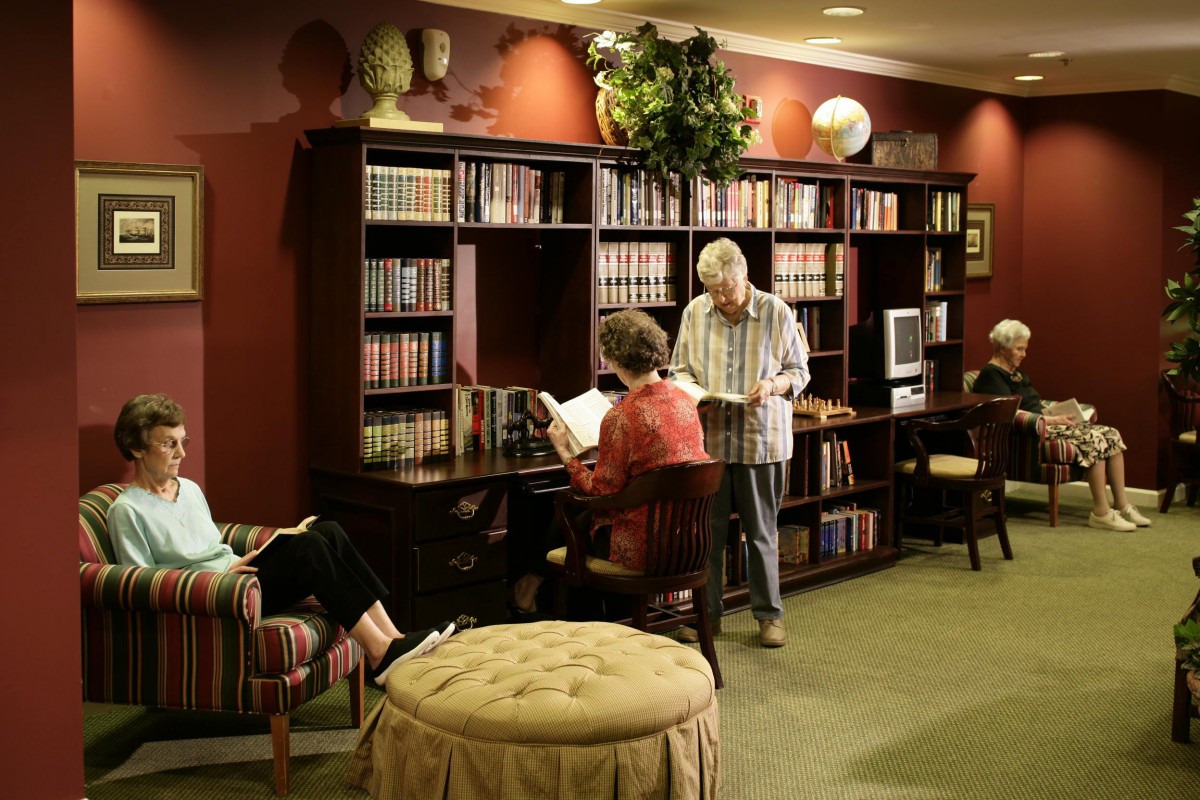 A cozy library setting with several people reading near a large bookshelf.