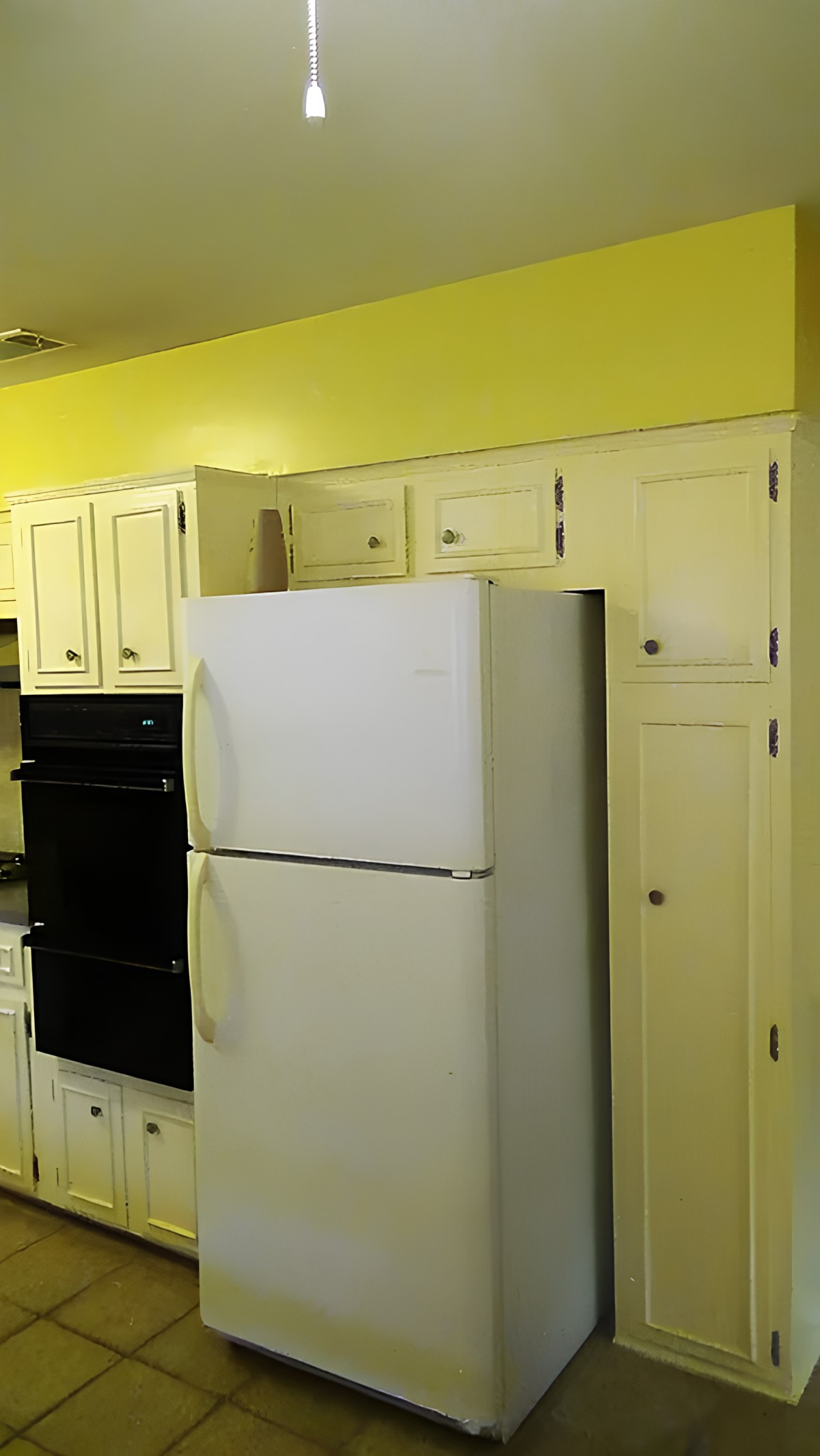 A kitchen with yellow walls, featuring a white refrigerator and cream-colored cabinets.