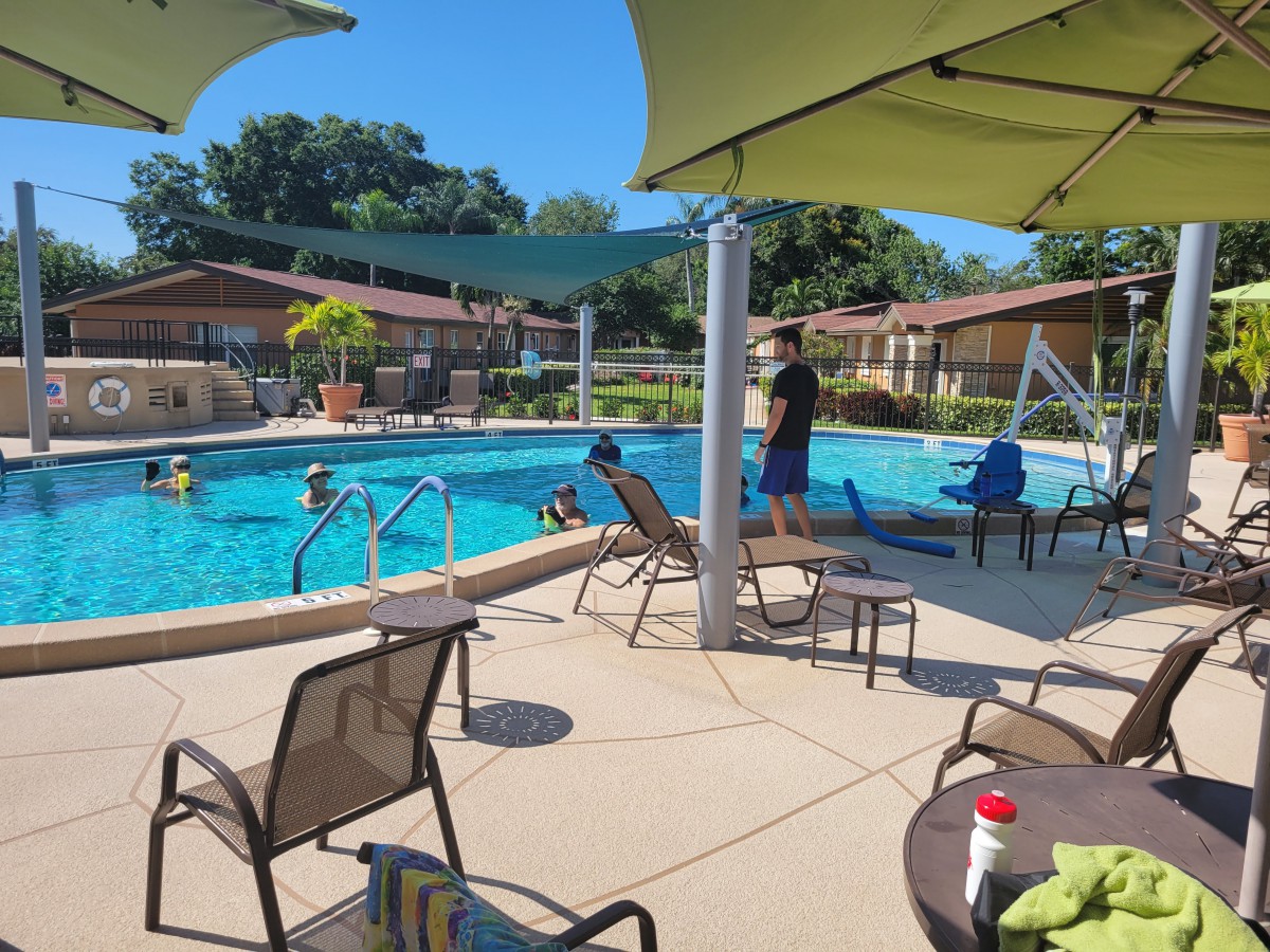 A sunny day at the outdoor swimming pool with people enjoying the water and relaxing by the poolside.