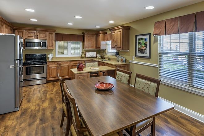 A warm and inviting kitchen with wooden cabinets and dining area, featuring modern appliances and a hardwood floor.