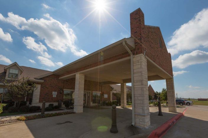A brick building with a covered entrance under a bright sunlit sky.