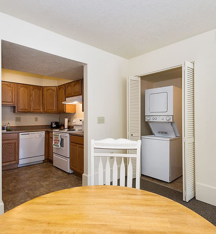 A cozy interior view featuring a kitchen area with wooden cabinets and a nearby laundry nook containing a stacked washer and dryer.