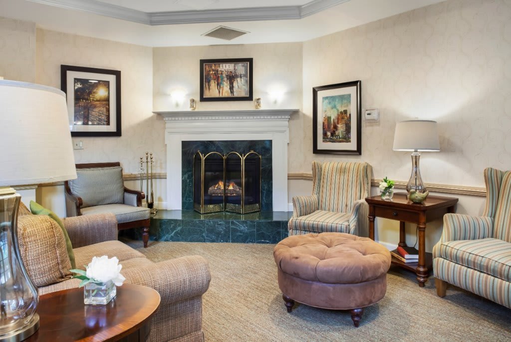A cozy living room with a fireplace, armchairs, and an ottoman.
