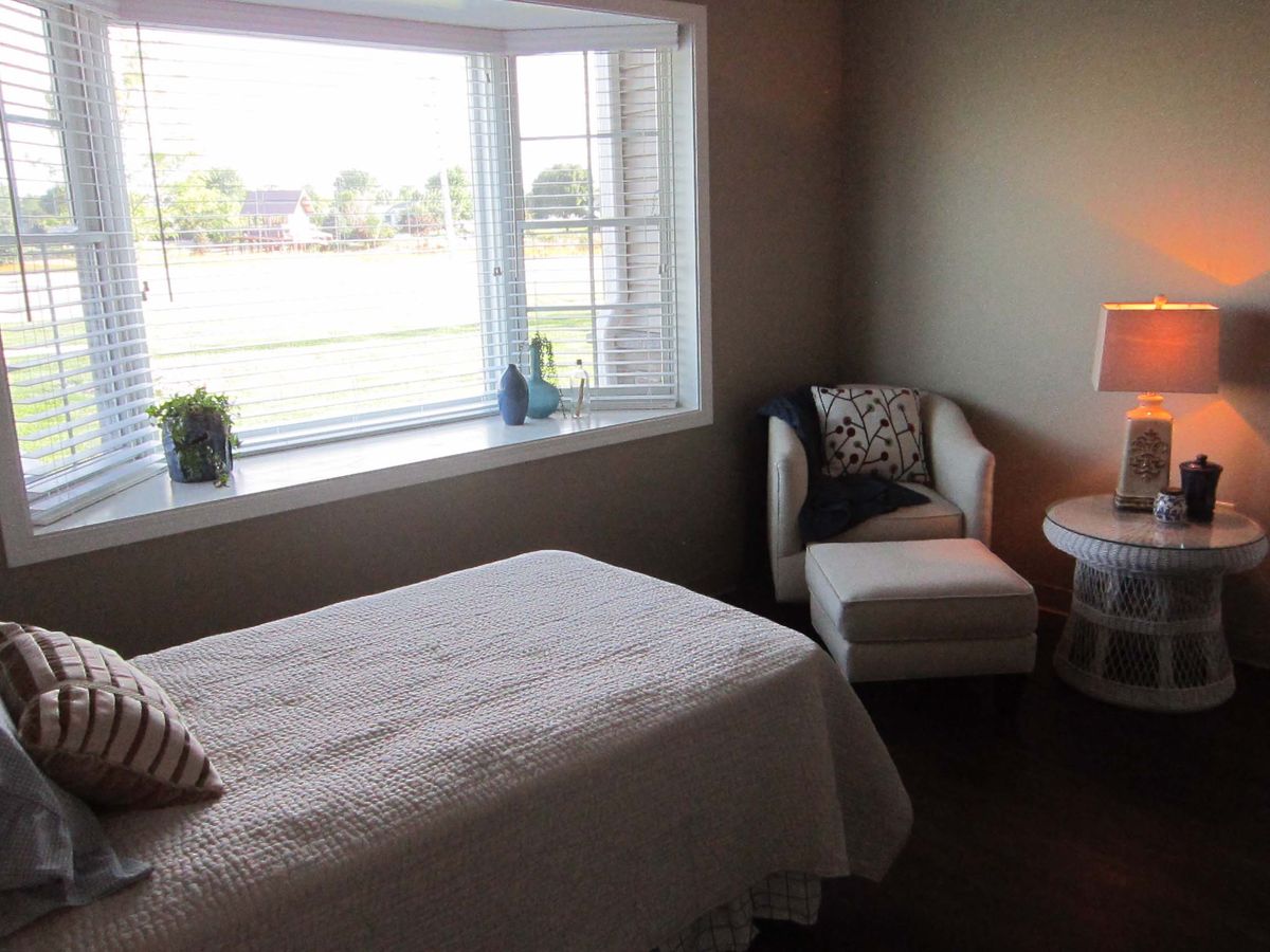 A cozy bedroom with a large window letting in natural light, featuring a bed and an armchair.