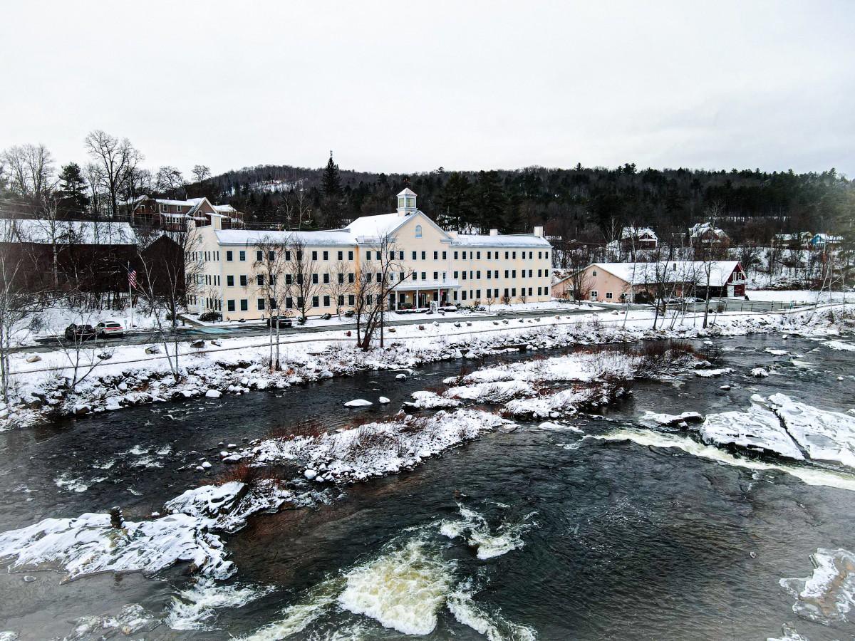A snowy river scene in a quaint town with buildings lining the water's edge.