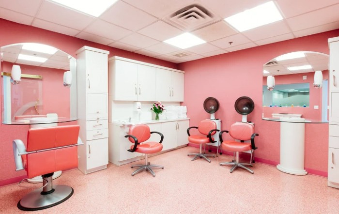 A brightly lit salon with pink walls, featuring styling chairs and hair dryers.