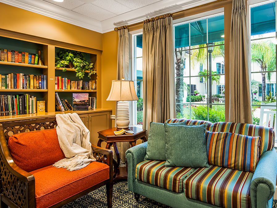 A cozy living room with vibrant sofas and a bookshelf, illuminated by natural light through the window.