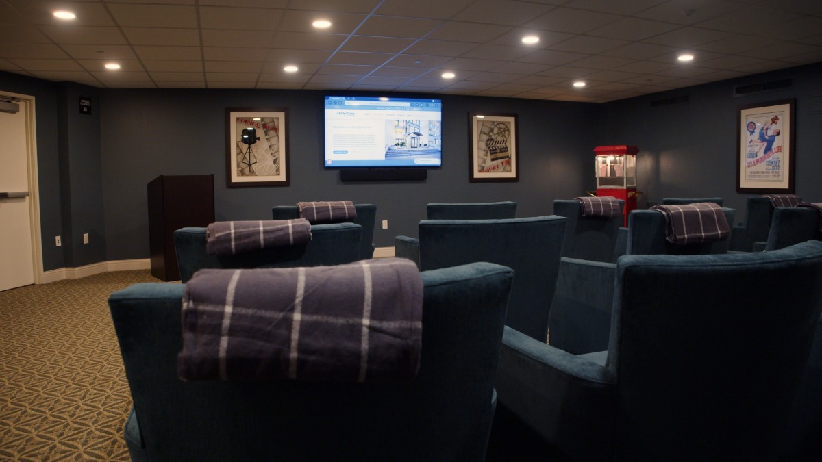 A cozy home theater setup with comfortable seating, a large projector screen, movie posters on the walls, and a popcorn machine in the corner.