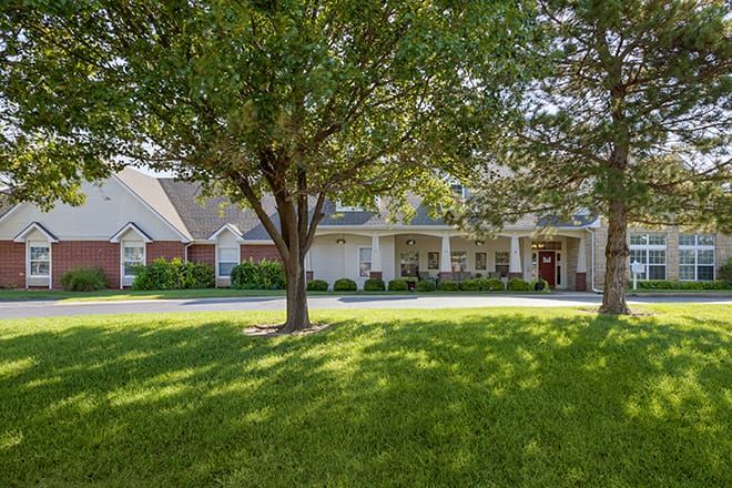 A picturesque suburban house with a well-maintained lawn and large trees casting shadows in the sunlight.