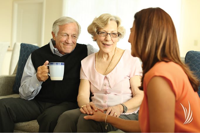 An elderly couple enjoys a warm conversation with a younger woman over tea.