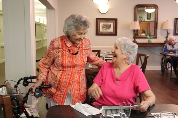 Two elderly women share a joyful conversation indoors.