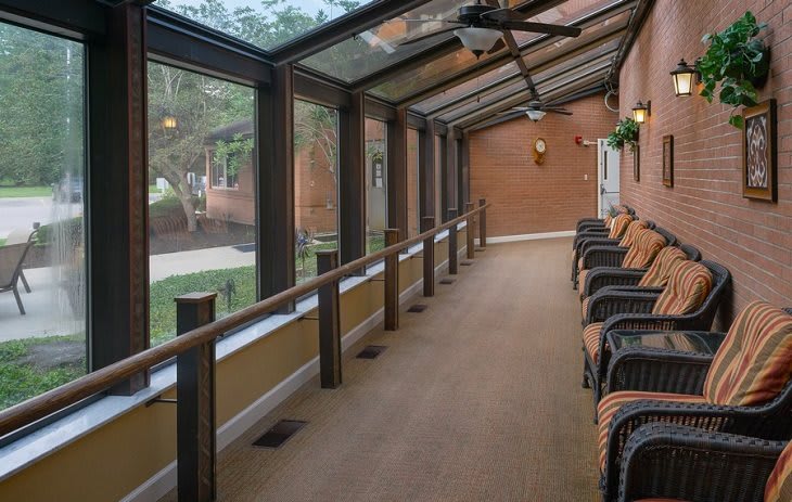 A sunlit hallway with large windows and a row of chairs.