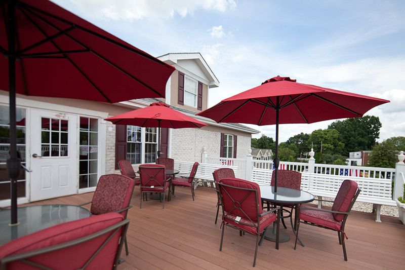 An inviting patio with red umbrellas over tables and chairs on a clear, sunny day.