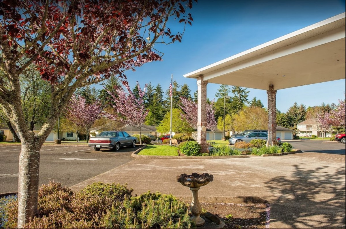 A well-maintained parking area with cars, surrounded by lush trees and a covered entrance to a building.