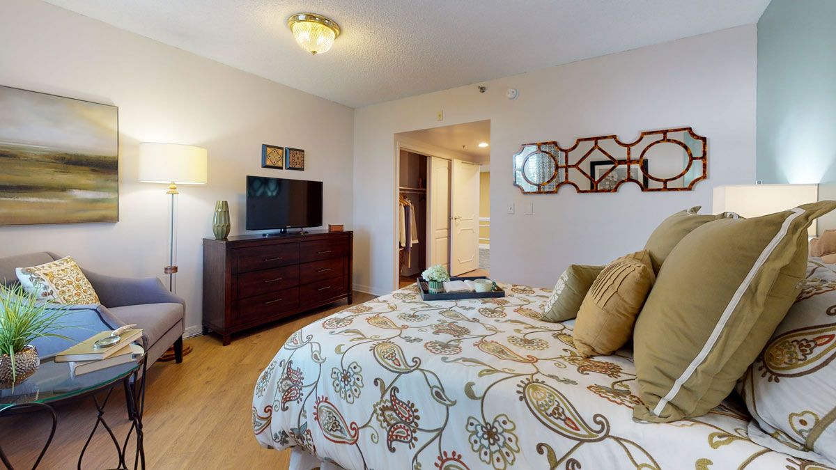 A cozy bedroom with elegant decor, featuring a comfortable bed, dresser, and mounted TV.