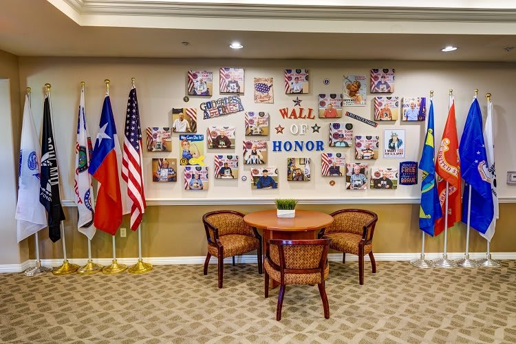 A Wall of Honor display featuring various flags, chairs, and a table in front of a collage of photos.